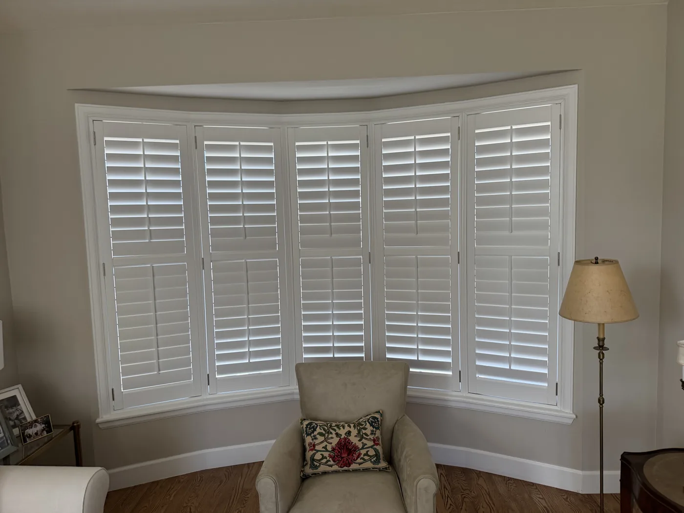White plantation shutters with closed louvers in a curved bay window, Howard's Draperies custom shutter installation